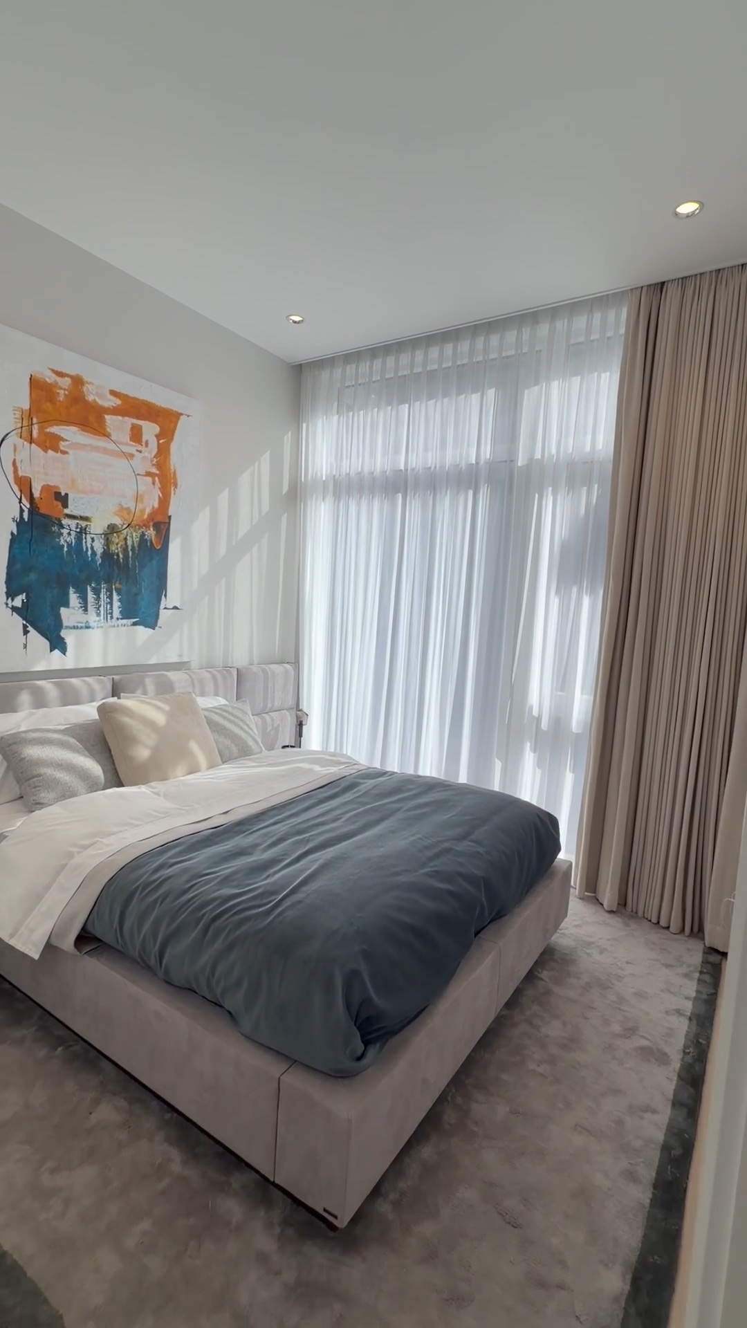 Blue bedding, a soft upholstered bed, and sheer window curtains